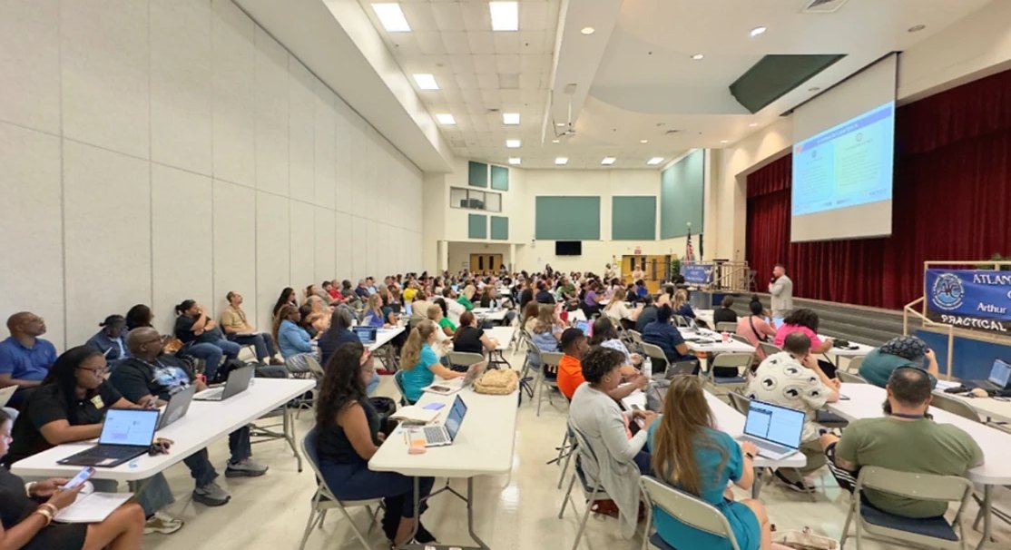 Wide view of the full room of AI Liaisons working on laptops during the kickoff presentation